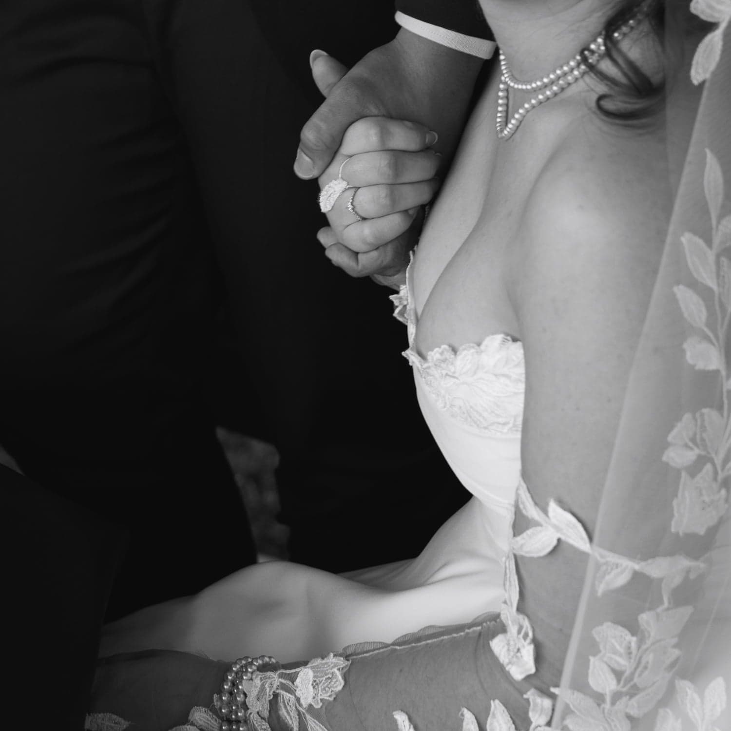 Black and white close-up of couple holding hands with pearl jewellery, wedding photography in Canberra.