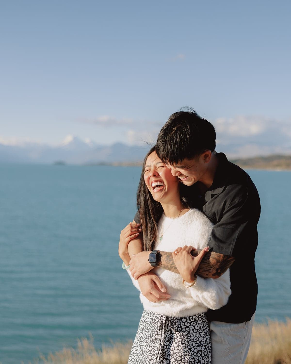 Couple laughing and embracing during surprise proposal photography at Lake Pukaki, New Zealand, with Mt Cook in background.